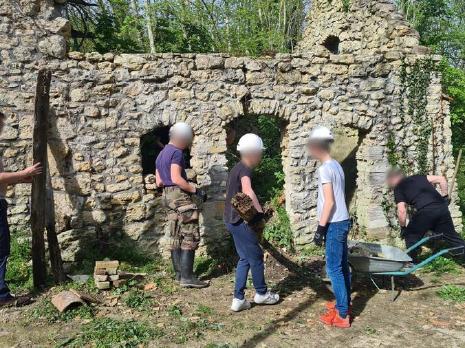 Jeunes avec casques et gants travaillant autour d'un petit batiment.